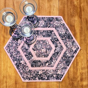 Peut inclure: Un chemin de table hexagonal avec un motif floral rose et noir. Le chemin de table est matelassé et fait de tissu.