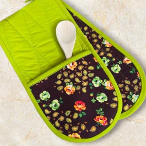 May include: Quilted oven mitts in lime green with a floral pocket. The pocket has a dark brown background with yellow paisley and colourful roses. A wooden spoon is placed inside the pocket.