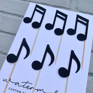 May include: Black glitter musical note cake toppers on wooden sticks. The note toppers are perfect for a music themed party or celebration.