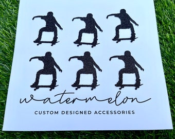 May include: Six black silhouette stickers of skateboarders on skateboards. The stickers are arranged in two rows of three. The stickers are on a white background. The text "watermelon CUSTOM DESIGNED ACCESSORIES" is at the bottom of the image.