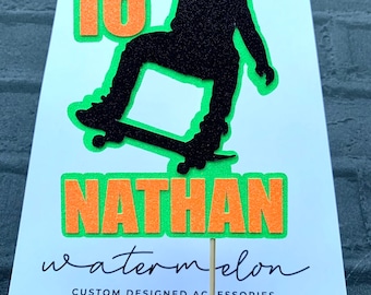 May include: A green and orange felt cake topper with a silhouette of a person skateboarding. The topper says "16" and "NATHAN" and "watermelon custom designed accessories".