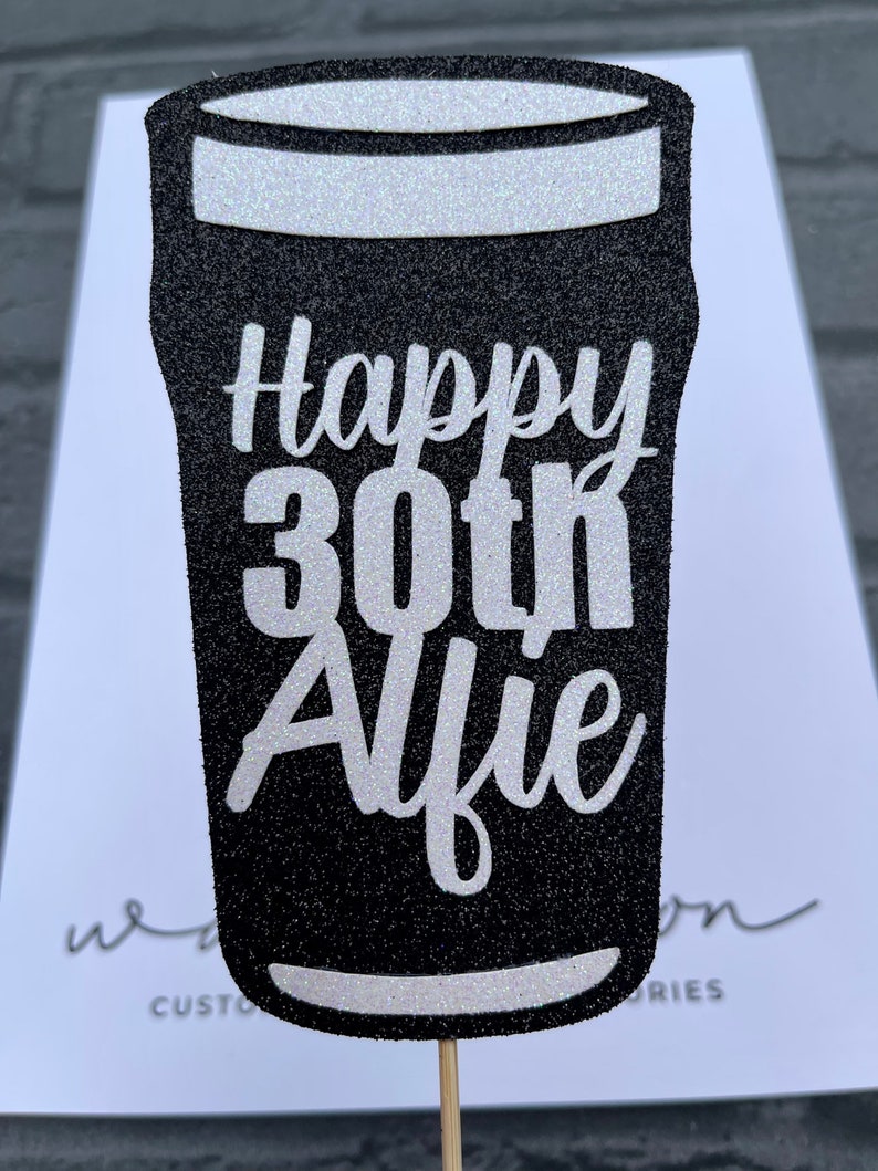 K&ouml;nnte beinhalten: Schwarzer und wei&szlig;er Glitzer-Kuchentopper in Form eines Bierglases mit dem Text "Happy 30th Alfie".