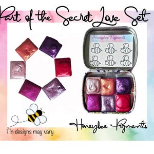 May include: Part of the Secret Love Set watercolor paint set in a tin with a bee design. The set includes six watercolor pans in shades of pink, purple, and red. The tin is labeled "Honeybee Pigments".