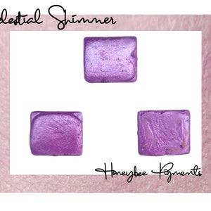 May include: Three square samples of Celestial Shimmer mica powder in a light purple color with a shimmery finish. The samples are arranged in a triangle shape on a white background. The text "Honeybee Pigments" is visible in the bottom right corner of the image.
