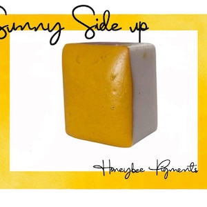 Op de afbeelding: Een vierkante blok gele aquarelverf met een witte rand. De verf is gelabeld met "Sunny Side Up" en "Honeybee Pigments".