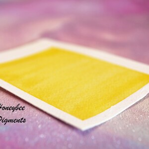 May include: A rectangular watercolour swatch in a bright yellow shade, set against a soft, blurred background. The paper has a white border and the text "Honeybee Pigments" is visible in the lower left corner.