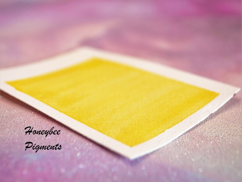 May include: A rectangular watercolour swatch in a bright yellow shade, set against a soft, blurred background. The paper has a white border and the text "Honeybee Pigments" is visible in the lower left corner.