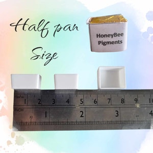 May include: Three white watercolor pans, measuring approximately 2 inches wide, labeled "Half pan Size". A ruler is placed below the pans for size reference. A gold foil wrapped watercolor pan labeled "HoneyBee Pigments" is shown above the pans.