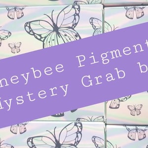 May include: A stack of small boxes with a butterfly design. The boxes are labeled "Honeybee Pigments Mystery Grab Bags".