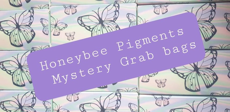 May include: A stack of small boxes with a butterfly design. The boxes are labeled "Honeybee Pigments Mystery Grab Bags".