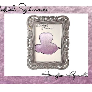 May include: A silver ornate frame with a pearl border, displaying a sample of "Celestial Shimmer" mica powder in a light purple color. The text "Celestial Shimmer" and "Honeybee Pigments" are visible in the image.