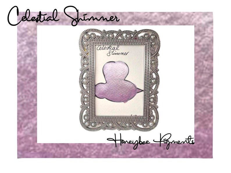 May include: A silver ornate frame with a pearl border, displaying a sample of "Celestial Shimmer" mica powder in a light purple color. The text "Celestial Shimmer" and "Honeybee Pigments" are visible in the image.