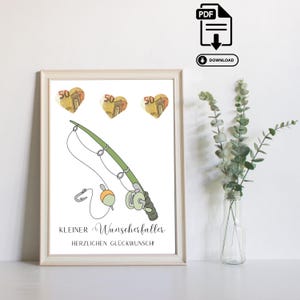 May include: Framed print with a green and white fishing rod illustration, a hook, and a reel. Above the rod are three heart-shaped currency images. The text reads "Kleiner Wunscherfüller" and "Herzlichen Glückwunsch!" at the bottom.