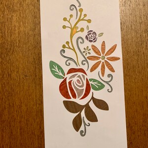May include: A paper cut-out design featuring a red rose with green leaves, a brown daisy with a yellow center, and a small purple flower. The design is on a white background.