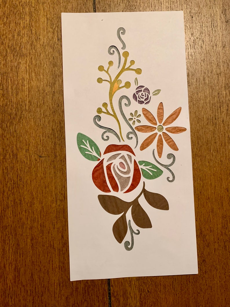 May include: A paper cut-out design featuring a red rose with green leaves, a brown daisy with a yellow center, and a small purple flower. The design is on a white background.