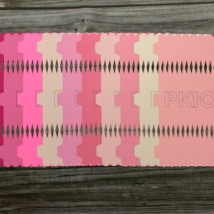 Puede incluir: Un conjunto de 16 cajas de papel rosa, rojo y crema con un borde festoneado y un patrón de diamantes. Las cajas están apiladas una encima de la otra y tienen el texto "PK10" impreso en la parte delantera.