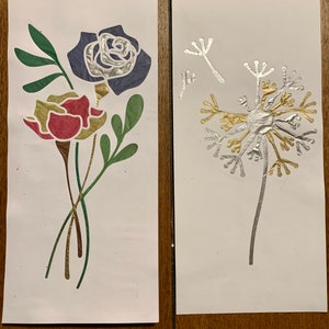 May include: Two cards with floral designs. The first card has a red and yellow flower with green leaves and a blue rose. The second card has a silver dandelion with gold accents.