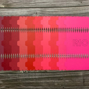 Puede incluir: Un conjunto de 16 muestras de color en tonos de rojo, rosa y burdeos. Las muestras están dispuestas en un degradado de oscuro a claro. La última muestra es un rosa brillante con el texto "R10" en blanco.