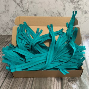 May include: A box filled with teal zipper closures. The zippers are all the same length and have a silver pull.