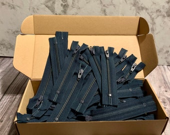 Könnte beinhalten: Ein Karton gefüllt mit einer großen Menge dunkelblauer Reißverschlüsse. Die Reißverschlüsse sind alle gleich groß und haben silberne Zipper.