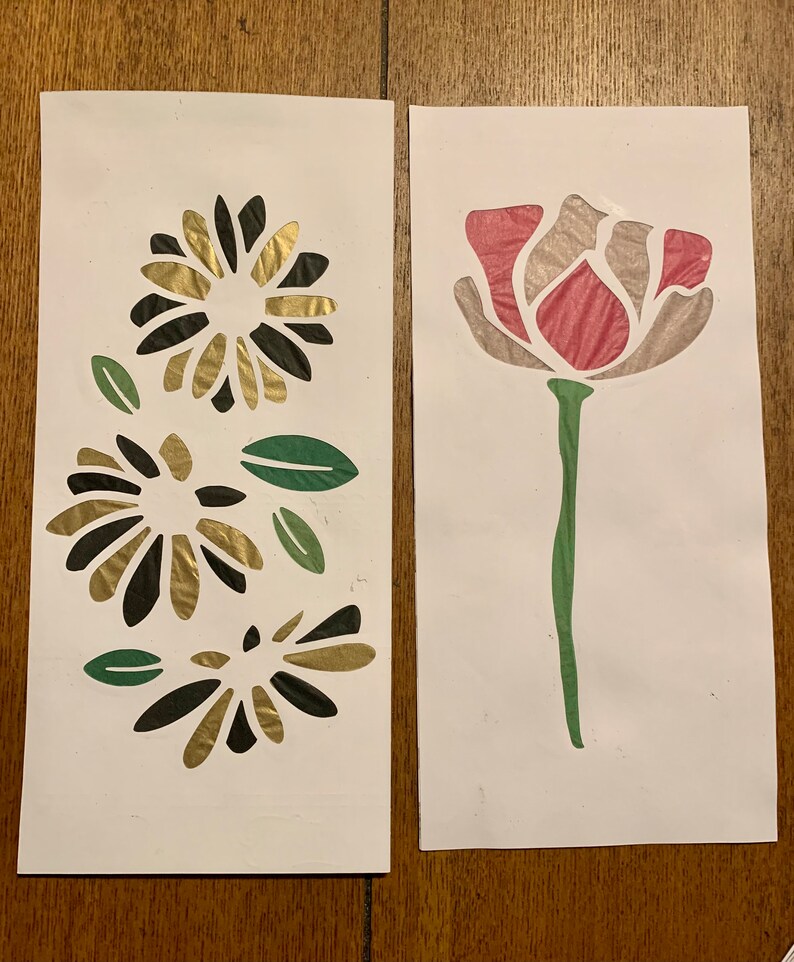 May include: Two cards with paper flower cutouts. The card on the left has three black and gold flowers with green leaves. The card on the right has a single pink flower with a green stem and leaves.