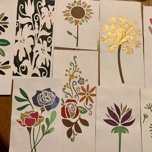 May include: A set of nine stencils featuring various floral designs. The stencils are made of a thin, flexible material and are perfect for creating intricate patterns on walls, furniture, and other surfaces. The designs include a sunflower, a dandelion, a rose, a lotus flower, and a variety of other floral motifs.