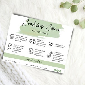Puede incluir: Una tarjeta blanca con el texto "Cookies Care" y un nombre comercial, junto con instrucciones de cuidado. La tarjeta tiene un fondo verde estilo acuarela e ilustraciones de galletas, un refrigerador y el sol. La tarjeta est&aacute; sobre una superficie blanca tejida.