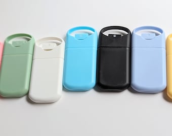Könnte beinhalten: Sieben kleine, nachfüllbare Sprühflaschen in verschiedenen Farben, darunter rosa, grün, weiß, blau, schwarz, hellblau und gelb. Die Flaschen haben einen transparenten Kunststoffkörper und eine schwarze Sprühdüse.