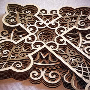 May include: A layered wooden art piece featuring an intricate, symmetrical design. The artwork is composed of multiple layers of laser-cut wood, creating a three-dimensional effect. The design incorporates geometric shapes and swirling patterns, with a natural wood color.