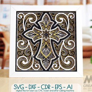 May include: A white frame with a black and gold intricate cross design inside. The cross is made up of multiple layers of cutouts, creating a 3D effect. The design is reminiscent of a stained glass window.