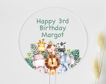 Può includere: Un cake topper rotondo e trasparente con la scritta "Happy 3rd Birthday Margot" in verde. La parte inferiore del topper presenta un'illustrazione ad acquerello di una giraffa, una zebra, un leone, un elefante, un ippopotamo e una scimmia circondati da foglie verdi.
