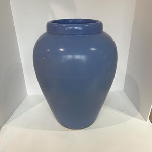 May include: A large, blue vase with a rounded body and a slightly flared rim. The vase has a smooth, matte finish and a simple, elegant design. It is a decorative item suitable for home decor.