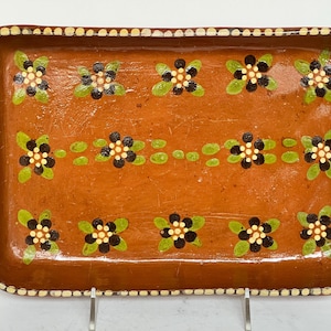 May include: Rectangular terracotta serving tray with a floral design. The tray features a brown base with hand-painted black and white flowers with green leaves. The rim is decorated with small, cream-colored dots.
