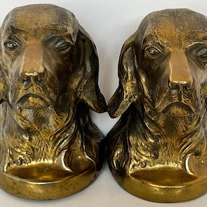 May include: Two antique brass dog head bookends. Each bookend features a detailed sculpture of a dog's head with long, floppy ears and a solemn expression. The bookends have a rich, aged patina, adding to their vintage appeal.