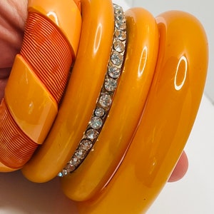 May include: Set of four orange plastic bangles, one with a row of clear rhinestones.