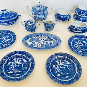May include: A collection of blue and white Willow pattern china. The set includes a teapot, sugar bowl, creamer, gravy boat, serving dishes, and plates. The dishes have a detailed landscape design.