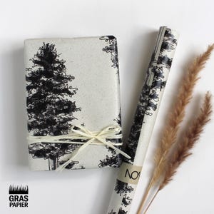 Könnte beinhalten: Eine rechteckige Geschenkbox und eine gerollte Geschenkpapierrolle, beide mit einem schwarzen Baumdesign auf cremefarbenem Hintergrund. Die Box ist mit Naturkordel gebunden. Auf dem Geschenkpapier steht das Wort "NO".