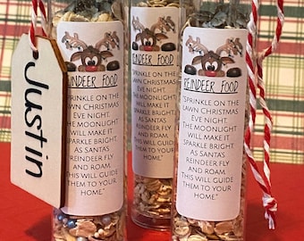 May include: Three clear tubes filled with reindeer food, each with a label featuring a cartoon reindeer and the text "Reindeer Food." The tubes are tied with red and white twine and a tag that says "Justin."