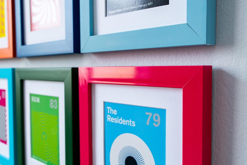 May include: A collection of framed art prints with colorful frames. The frames are in various colors, including red, blue, and green. The prints feature graphic designs and text, including "The Residents 79".