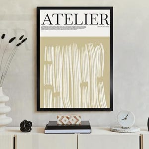 May include: A framed art print with the word "ATELIER" in black letters. The artwork features a beige background with vertical white brushstrokes. A white vase with black stems and a decorative clock are on a white cabinet.