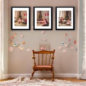 May include: Three framed pictures hang on a wall above a wooden chair and patterned rug. The pictures show a Christmas tree and a person with a child. Decorative paper cutouts of birds and flowers adorn the wall. The chair has a pink cushion.