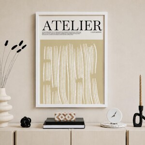 May include: A framed art print with the word "ATELIER" in black text. The artwork features vertical white brushstrokes on a beige background. Decorative items include a vase with dried flowers, a black sculpture, and a clock.