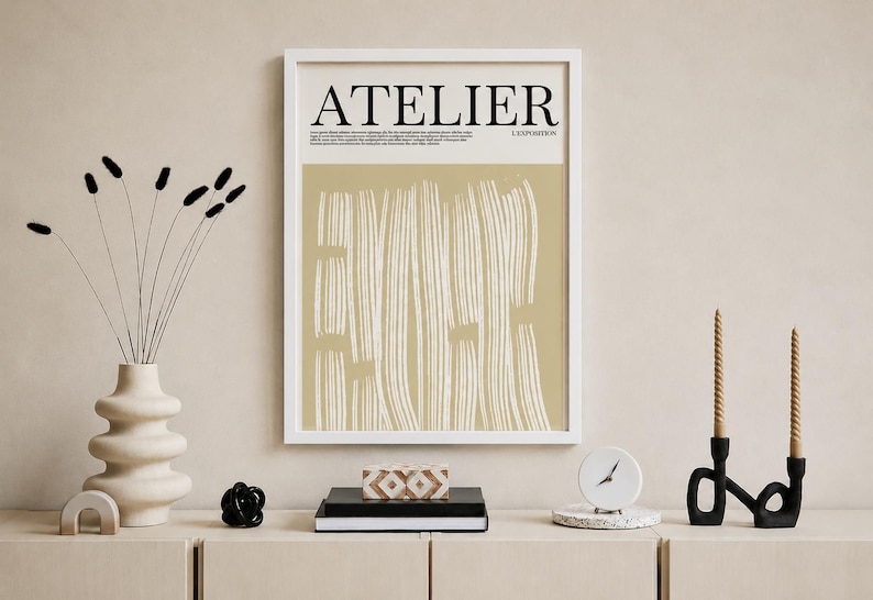 May include: A framed art print with the word "ATELIER" in black text. The artwork features vertical white brushstrokes on a beige background. Decorative items include a vase with dried flowers, a black sculpture, and a clock.