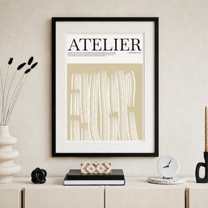 Puede incluir: Una impresión artística enmarcada con la palabra "ATELIER" en letras negras. La impresión tiene un fondo beige con líneas verticales blancas. Un jarrón con flores secas, un reloj y velas están sobre una superficie de madera.