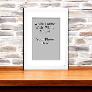 Könnte beinhalten: Weißer Bilderrahmen mit weißem Passepartout auf einer Holzoberfläche. Der Rahmen trägt den Text "White Frame With White Mount Your Photo Here".