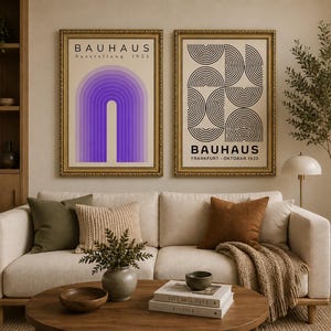 May include: Two framed Bauhaus art prints above a cream sofa. The left print has a purple arch design, the right a black and white geometric pattern. The gold frames complement the room's decor, including cushions and a wooden coffee table. The text 'BAUHAUS' is visible.