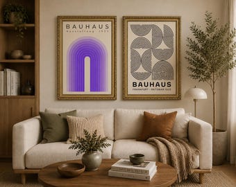 Op de afbeelding: Twee ingelijste Bauhaus kunstprints boven een crèmekleurige bank. De linker print heeft een paars boogontwerp, de rechter een zwart-wit geometrisch patroon. De gouden lijsten passen bij de kamerdecoratie, inclusief kussens en een houten salontafel. De tekst 'BAUHAUS' is zichtbaar.