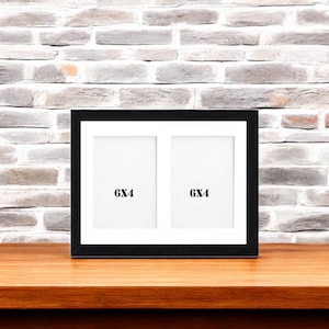 May include: Black picture frame with two 6x4 inch openings. The frame is on a wooden table.