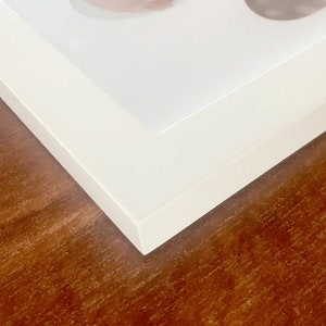 May include: Close-up of the corner of a white picture frame, showing the smooth, white surface and the clean lines of the frame.