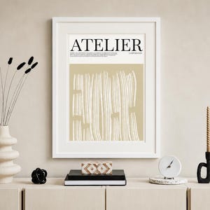 May include: A framed art print with the word "ATELIER" in black. The artwork features vertical white lines on a beige background. A vase with black stems, candles, and decorative objects complete the scene.